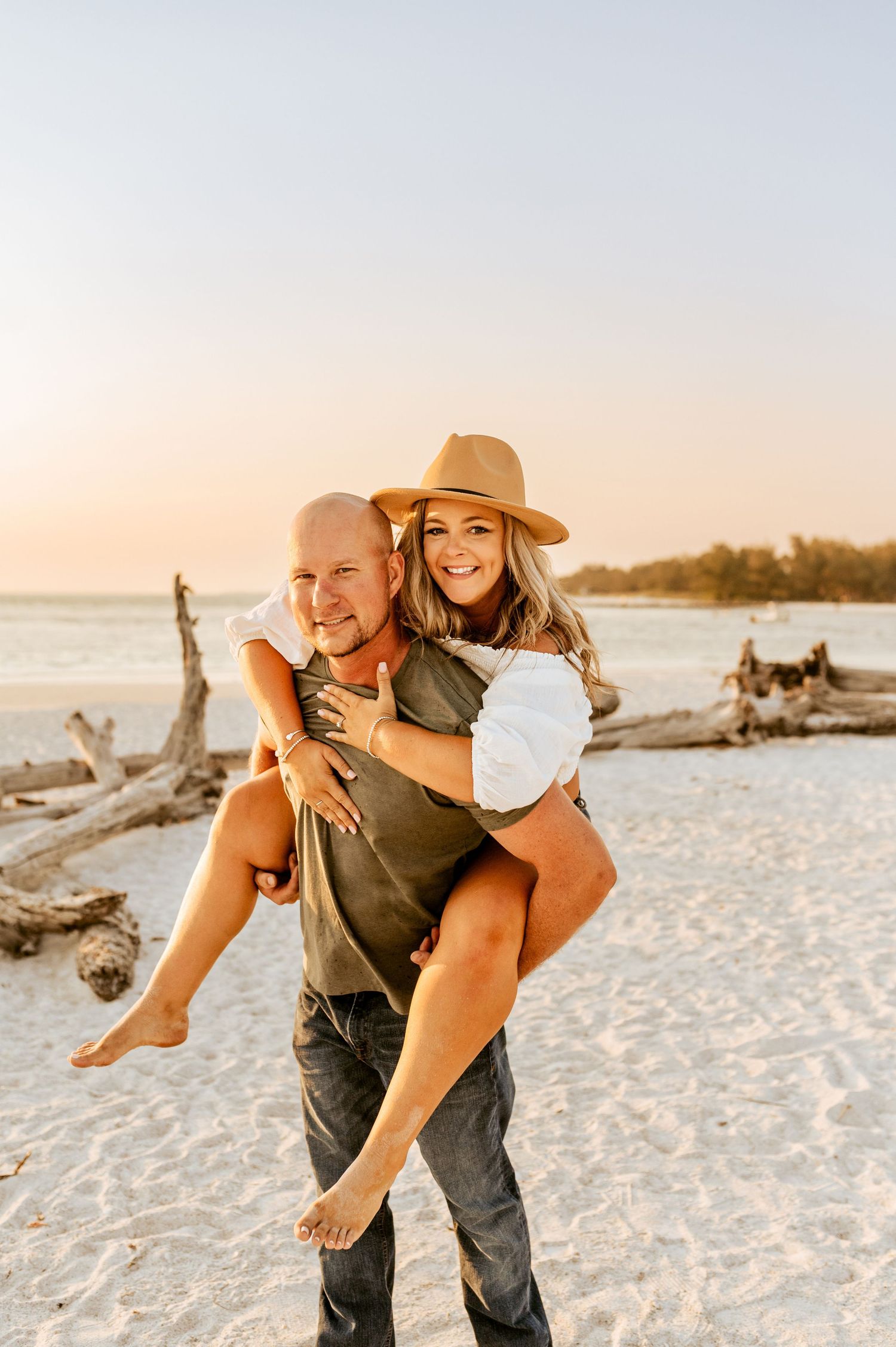 Carefree couple having fun with piggyback ride on sandy beach during golden hour.