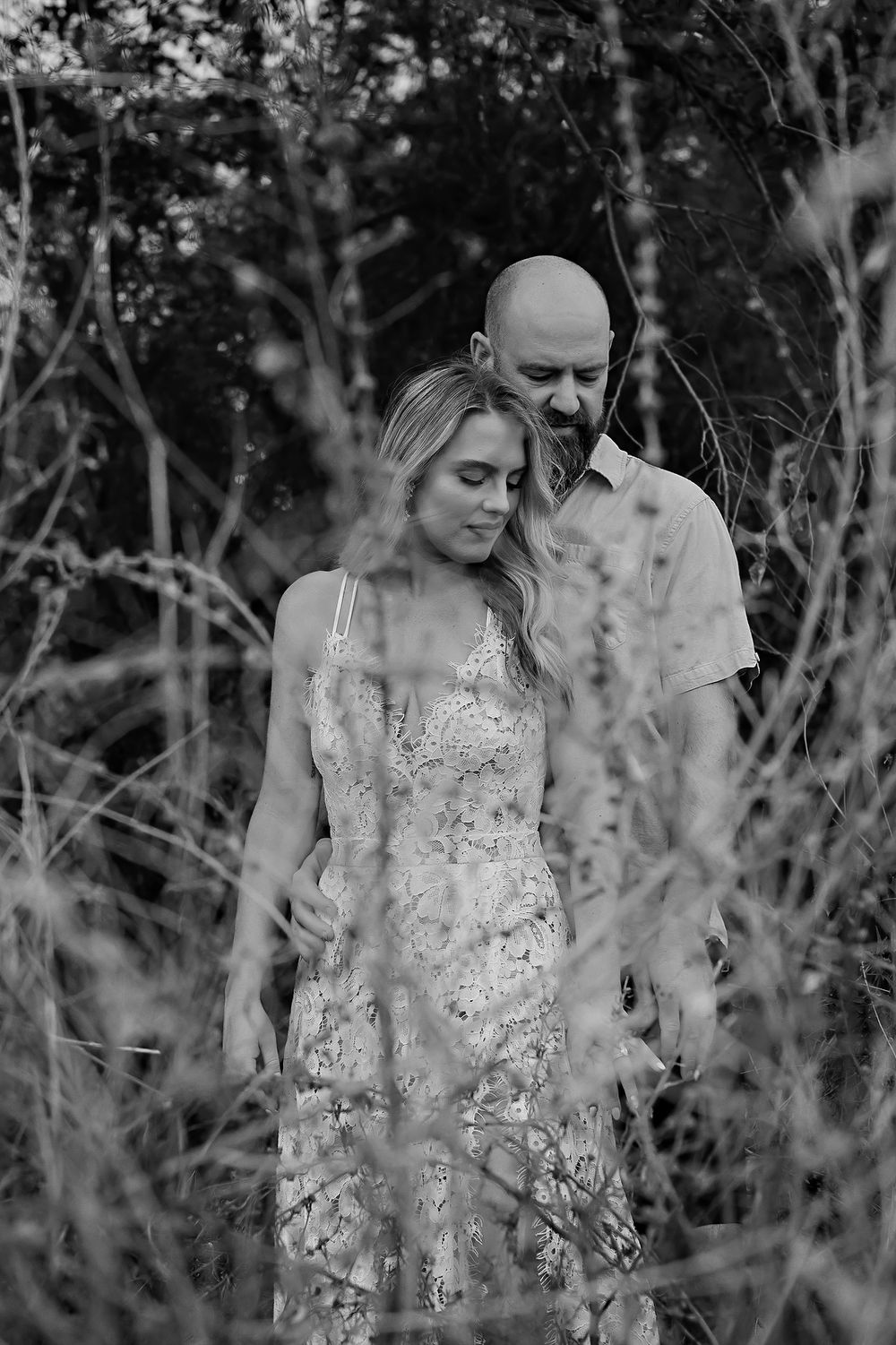 A romantic black and white engagement photo series showing a couple among branches and foliage.