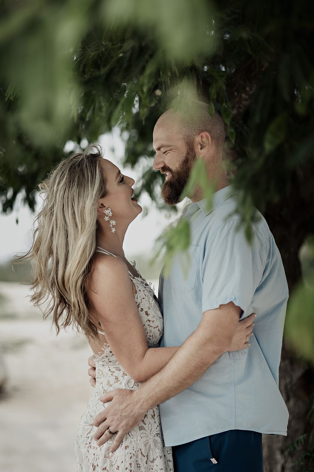 A romantic couple embraces under lush tree branches while sharing tender moments in a series of photos.