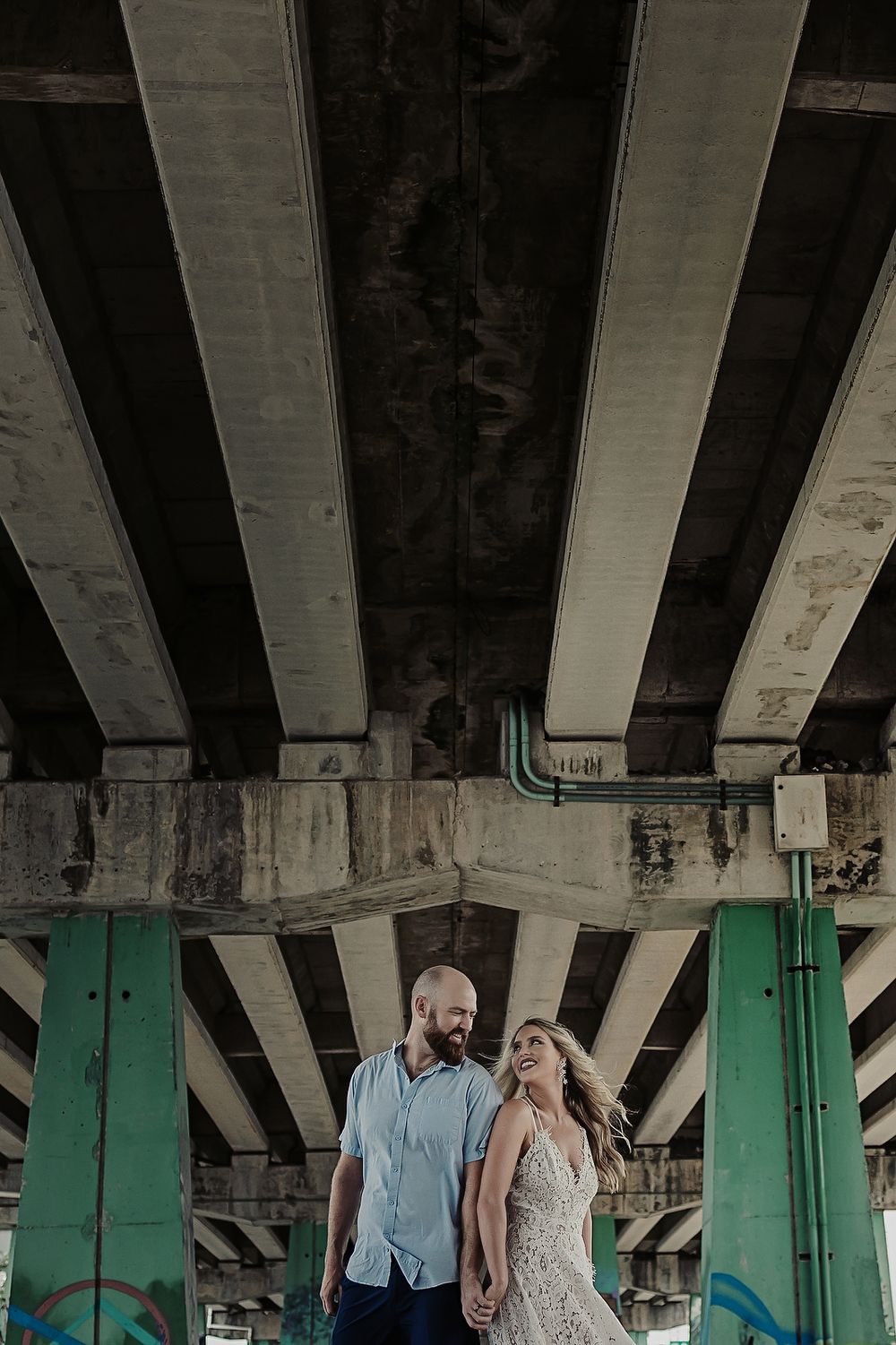 Couple laughing under an overpass with urban graffiti pillars, part of their Playa del Carmen honeymoon shoot.