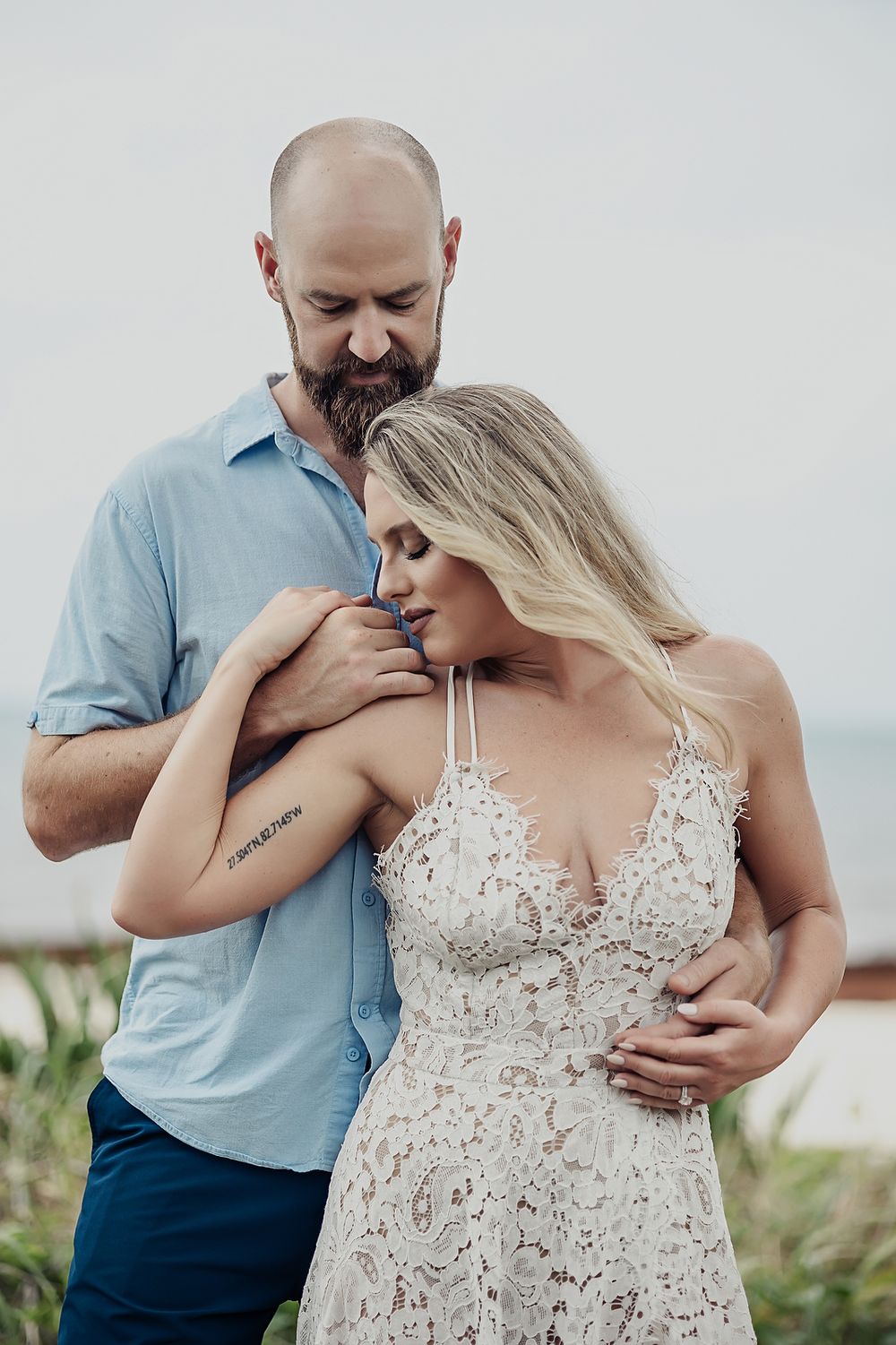Romantic coastal engagement photo session capturing intimate moments in a white lace dress and light blue shirt.