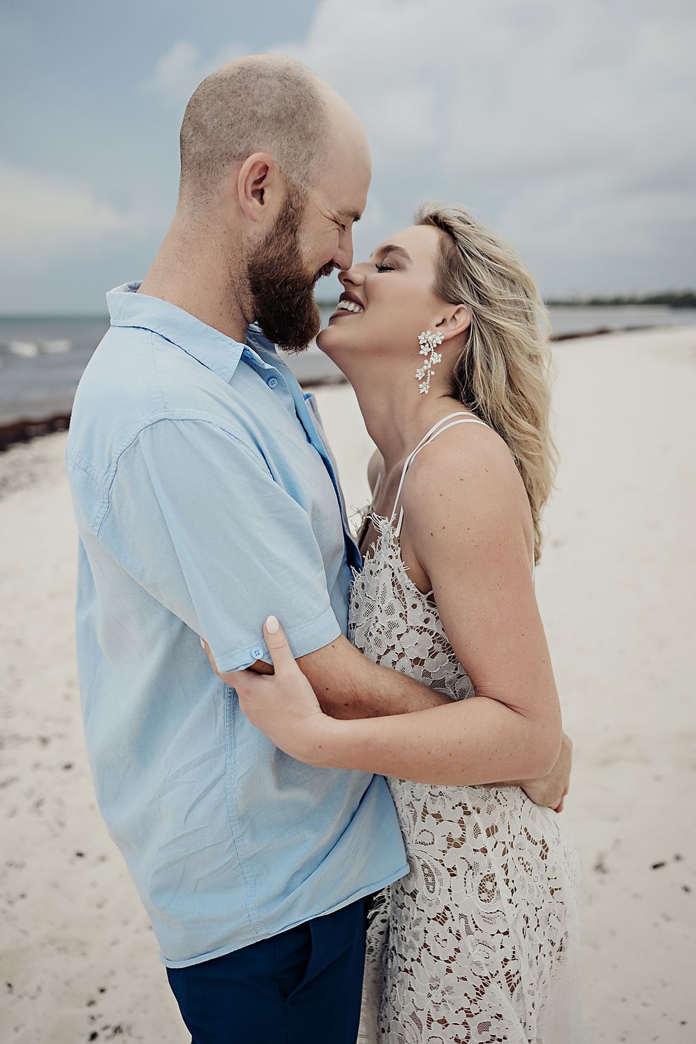 A romantic beach side portrait of a couple sharing an intimate moment wearing light blue and floral attire.