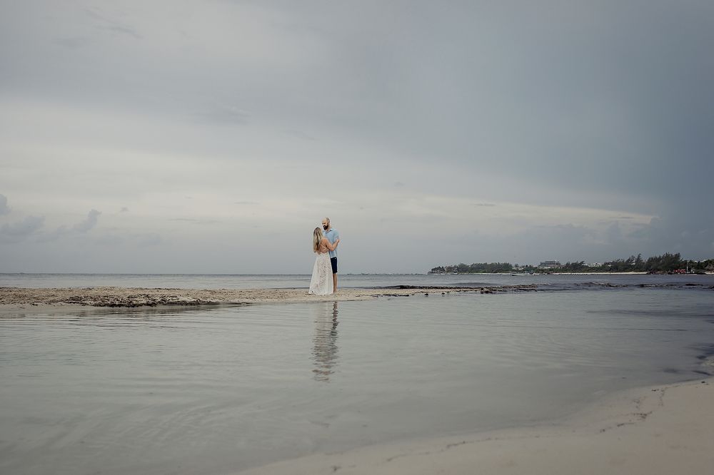 Couple stands in the distance at the edge of the water, their reflection visible in the calm sea in Playa del Carmen.