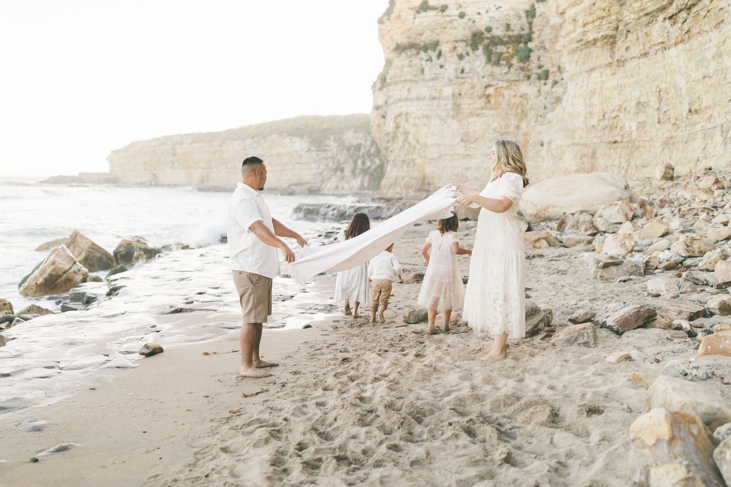 Couple and dogs stand on rocky beach near white limestone cliffs at sunset captured by Chelsee Rawe Photography.