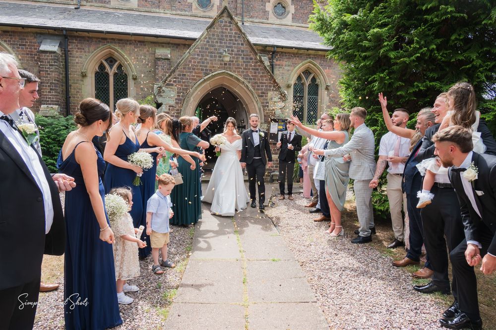Well-wishers throw confetti at a couple exiting a St Peters church through a gothic archway on their wedding day.