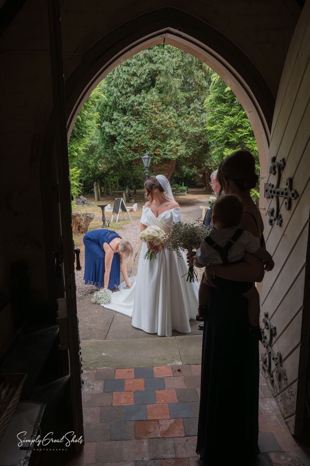 A wedding ceremony moment captured through a gothic church doorway framing a bridal scene with bridesmaids on a stone patio.