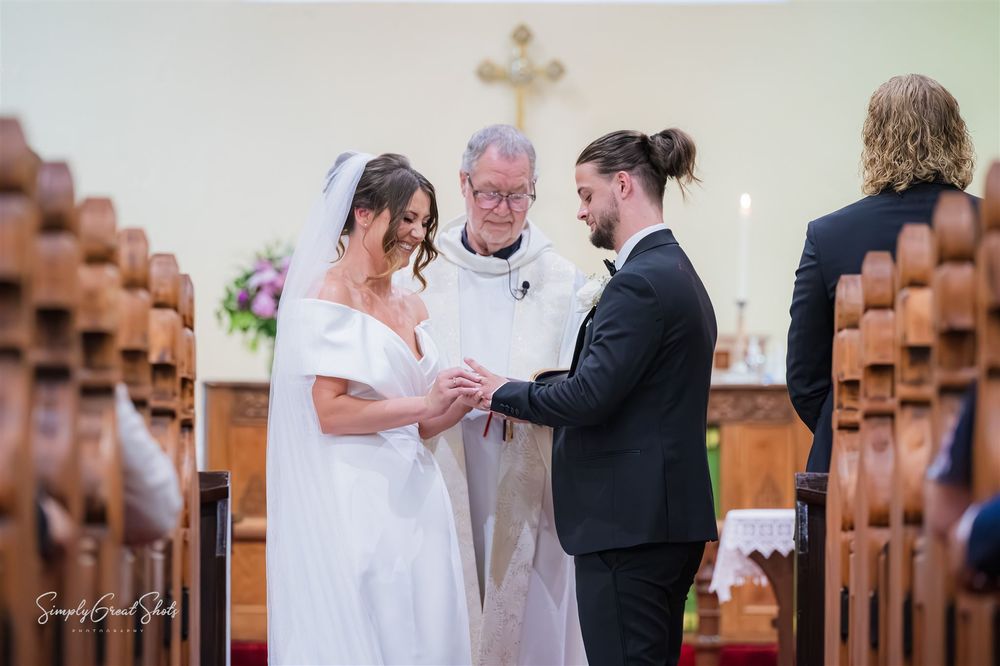 A wedding ceremony taking place in a church with wooden pews and a minister officiating the exchange of rings.