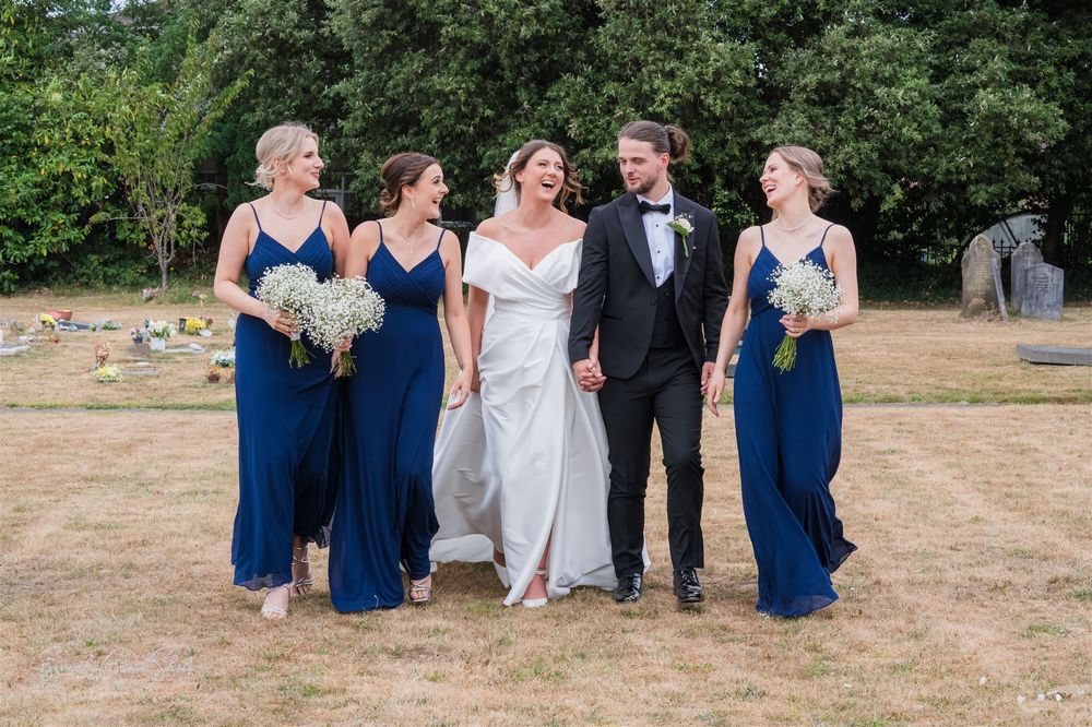 Wedding party members in navy blue and white attire walk together on a sunny lawn during an outdoor celebration.