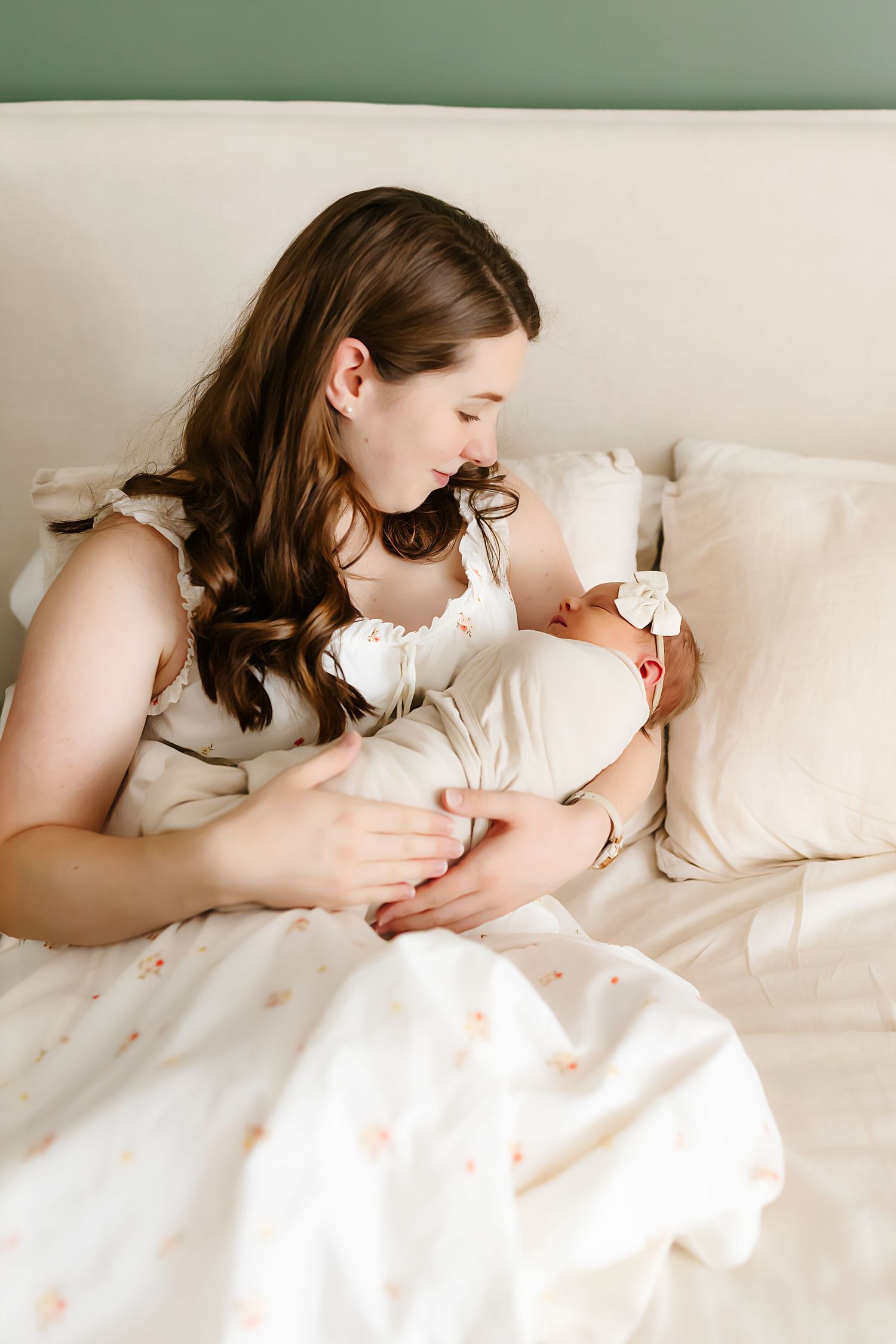 A gentle parenting moment on a white bed with soft pillows and linens in natural lighting.