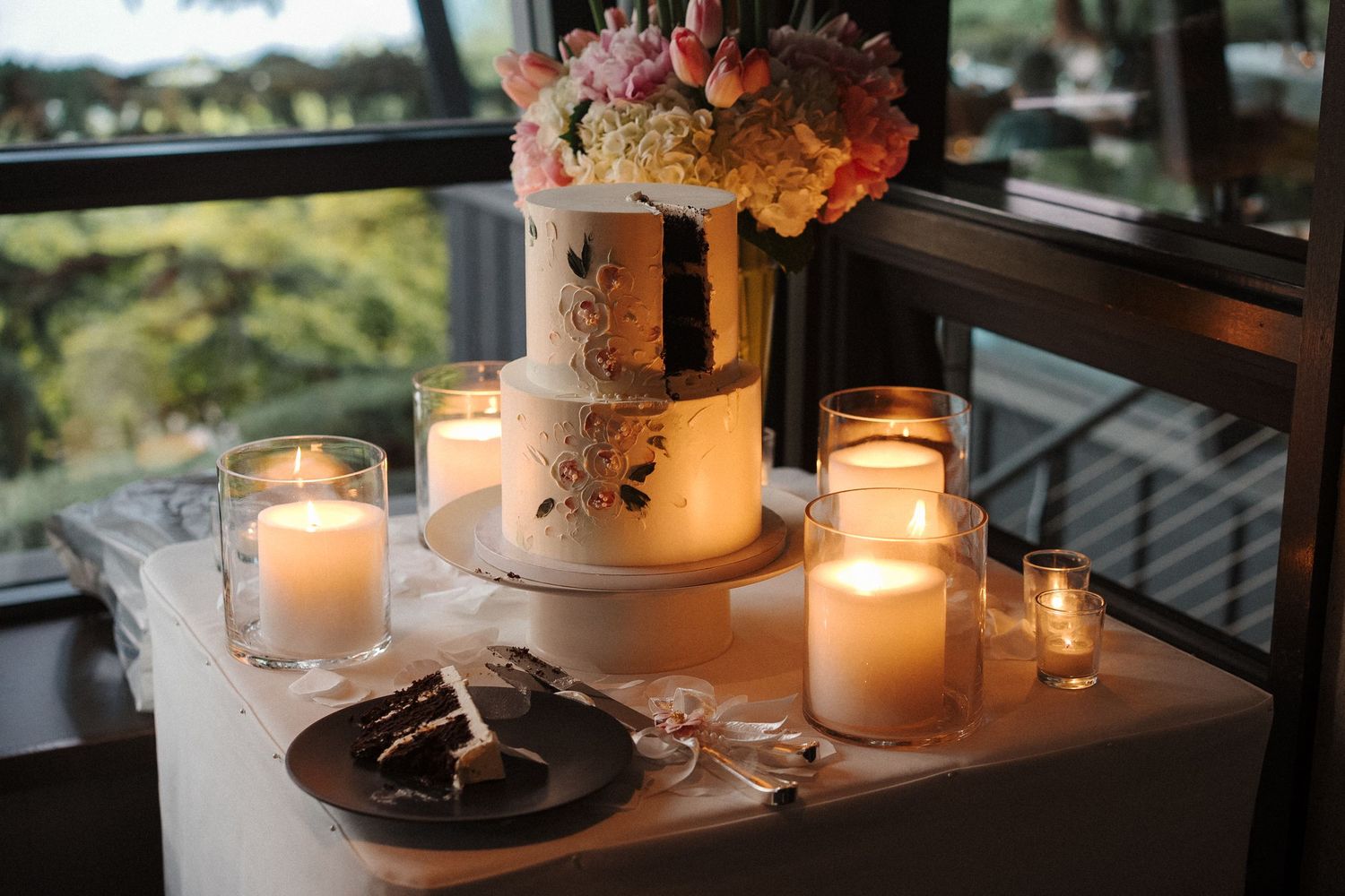 Illuminated white candles in glass jars create a romantic ambiance alongside delicate floral arrangements on dark surfaces.