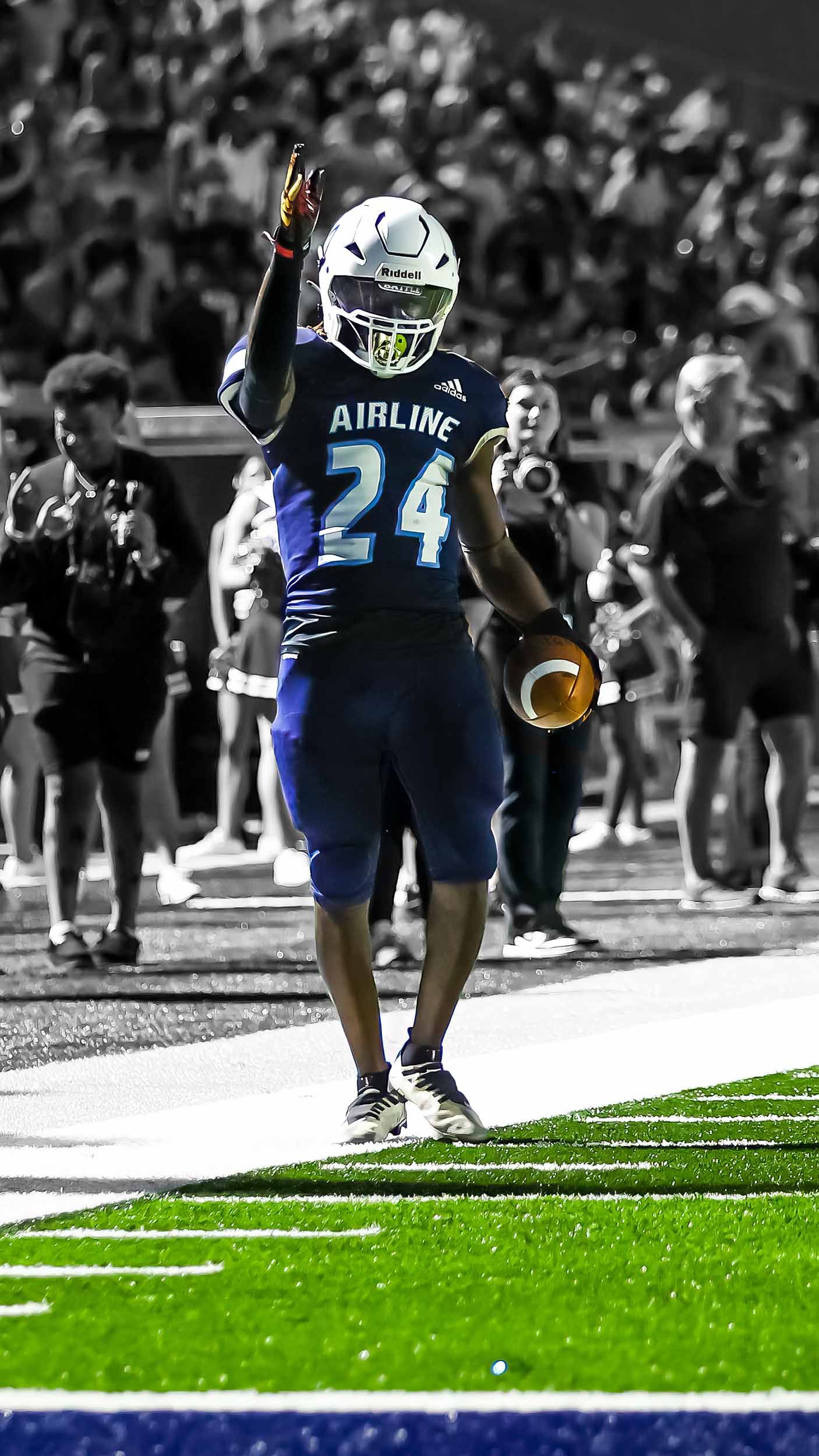 Football player wearing Airline jersey number 24 celebrates on the field with raised hand while holding ball.
