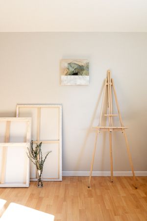 Minimalist art studio setup with wooden easel and blank canvases against white wall with hardwood flooring.