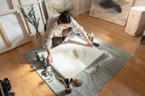 Artist working on canvas in bright studio space with wooden floors and natural lighting.