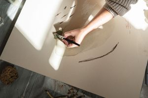 Artist's hand drawing a curved line on paper with natural sunlight casting dramatic shadows on the surface.