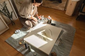 Artist drawing in a sketchbook with sunlight streaming through window onto a gray carpet.