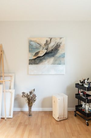 Modern living room corner with wooden floors, minimalist wall art, and wooden easels displaying abstract paintings.