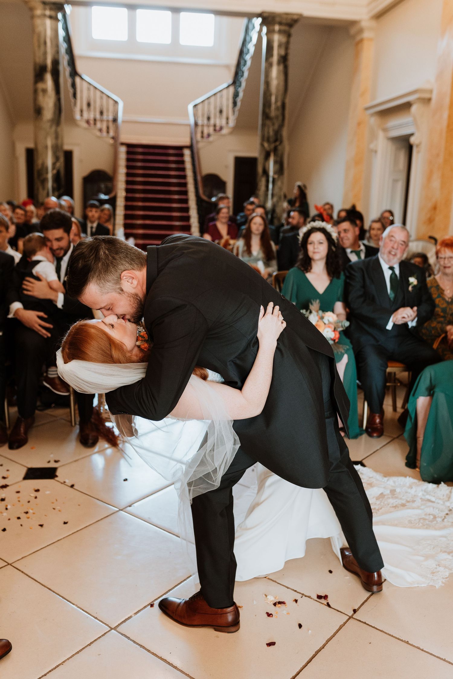 A romantic dip kiss for first kiss at an small wedding ceremony with guests watching in the background.