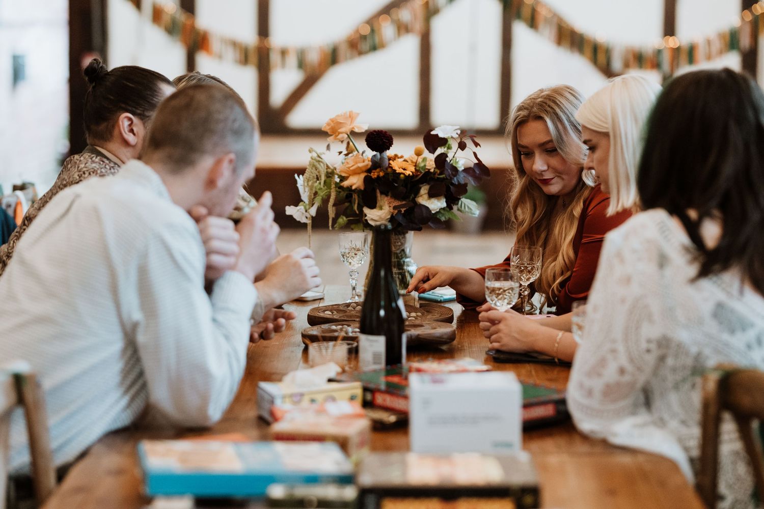 Rustic wooden table with guests playing board games and celebrating at a wedding reception in a cozy barn setting.