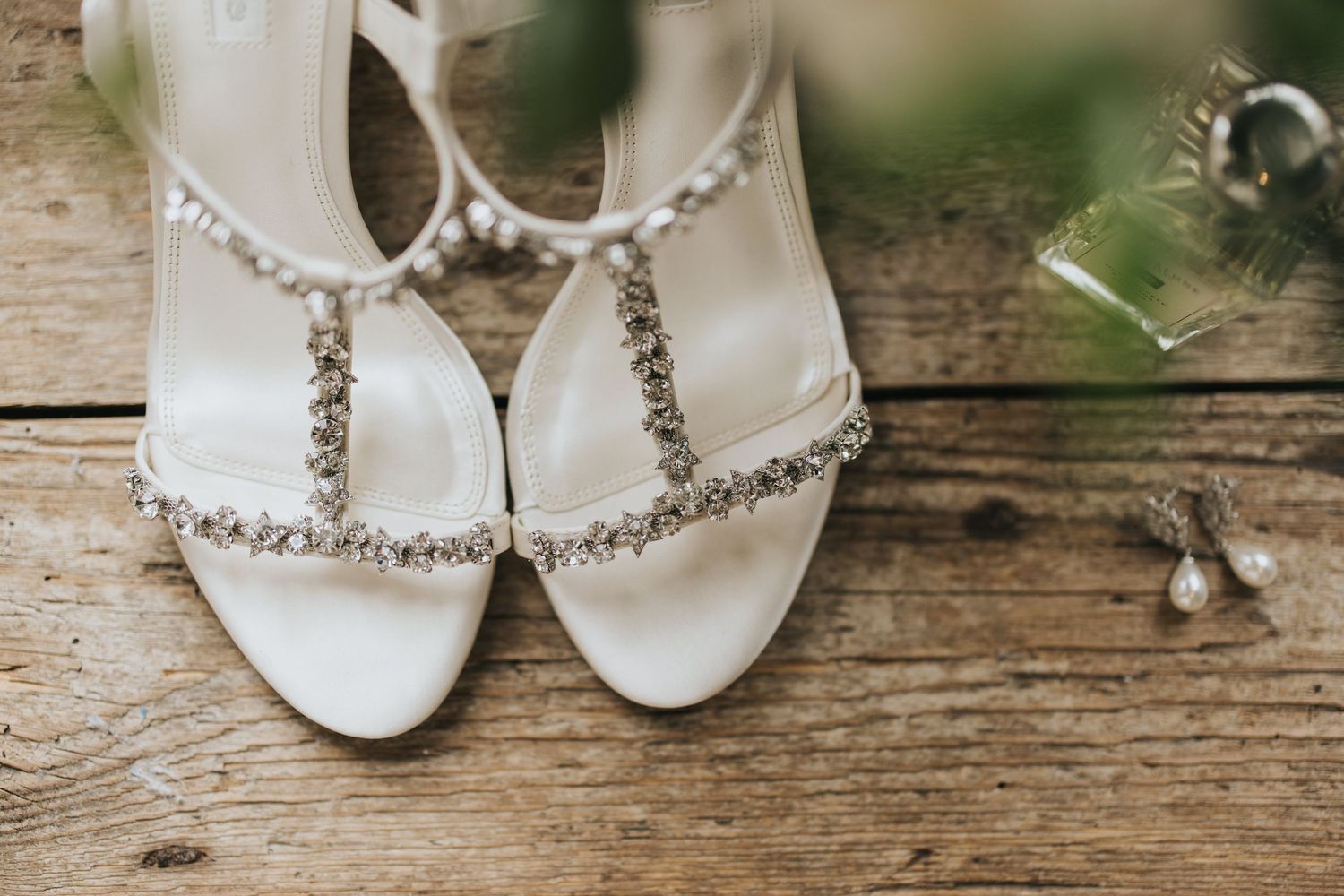 Elegant white bridal sandals with crystal embellishments displayed on rustic wooden planks.