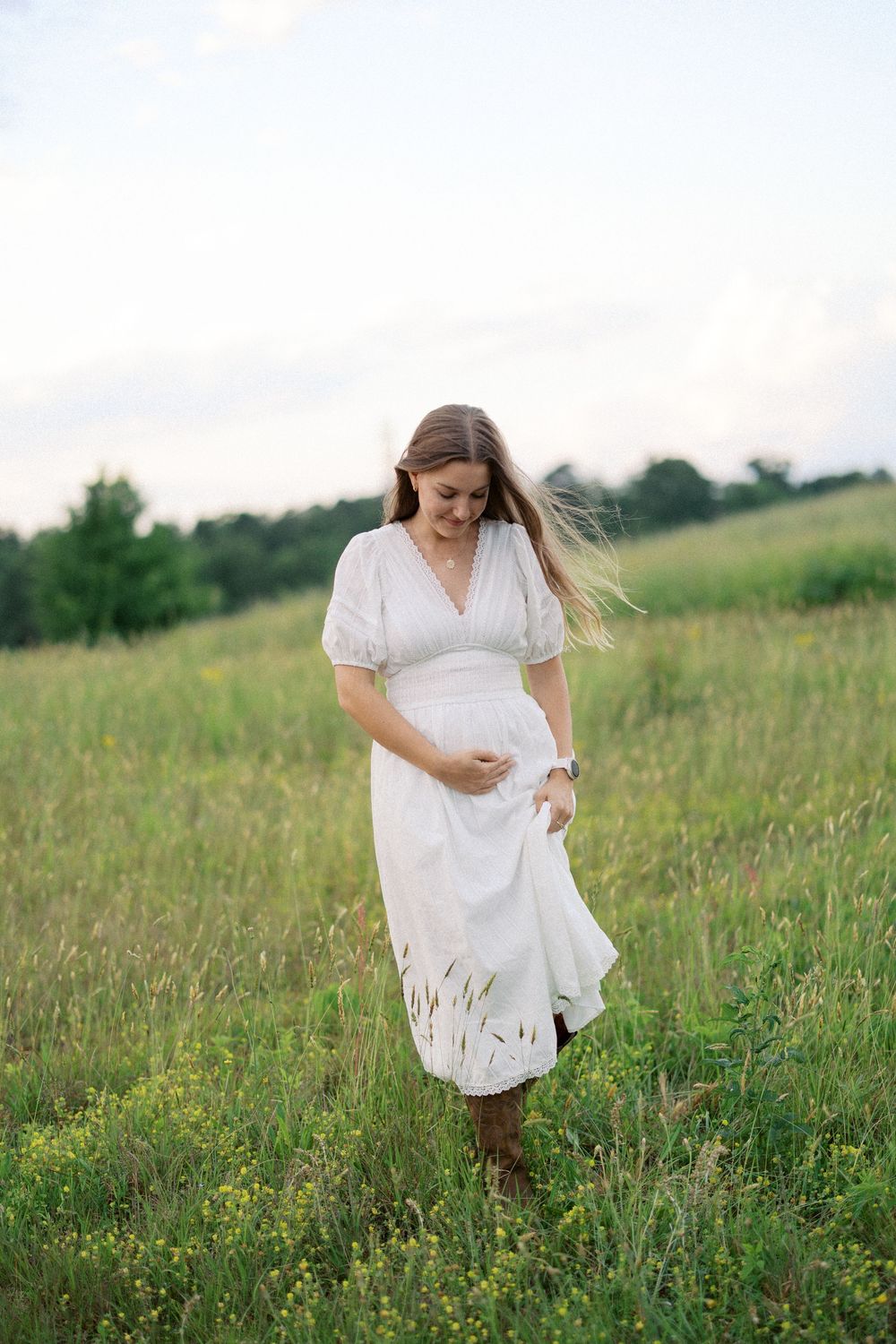 A woman in a flowing white dress stands in a wildflower meadow during golden hour.
