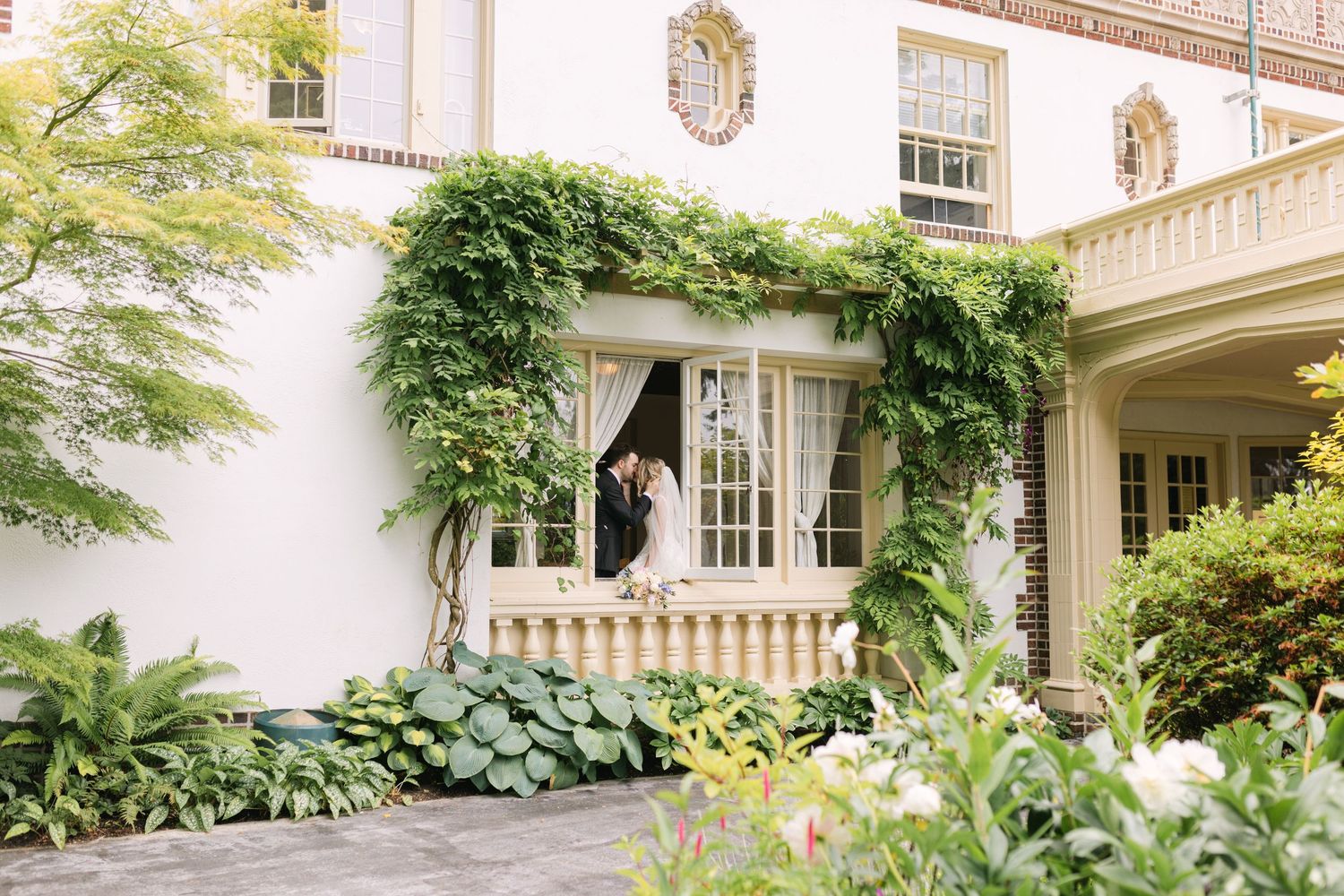 Elegant white mansion with French doors framed by lush green ivy and manicured garden landscaping.