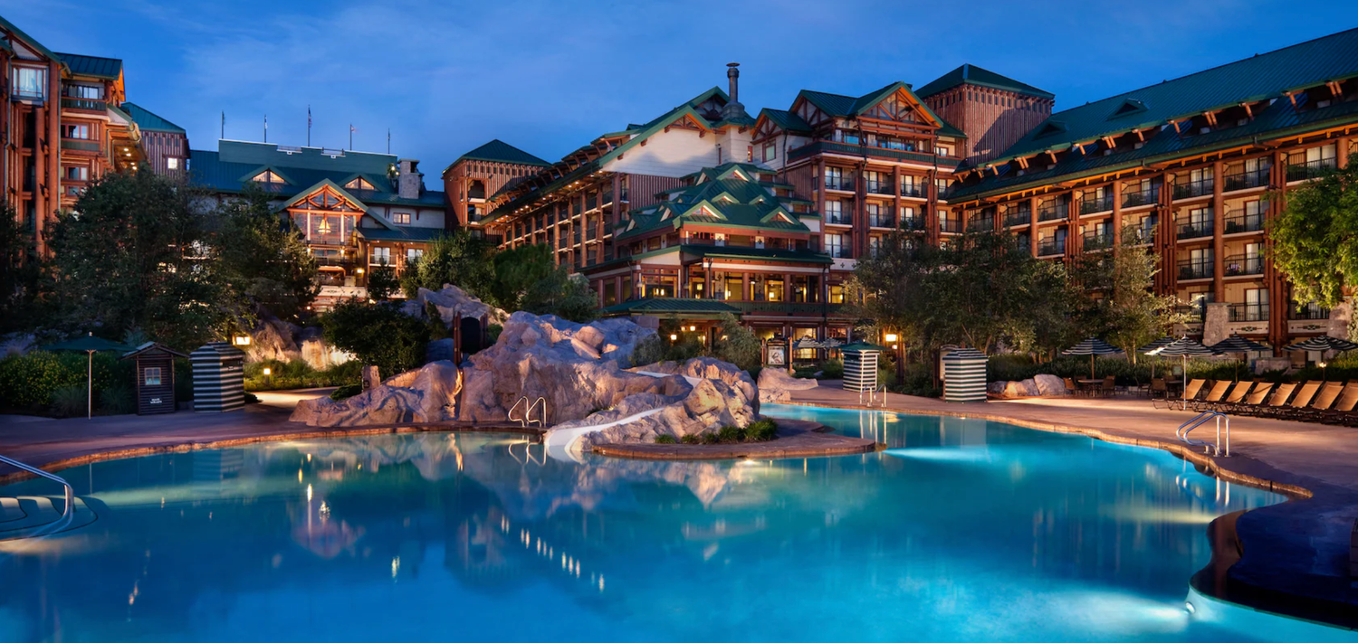 Illuminated Wilderness Lodge resort pool at twilight with rockwork and surrounding buildings.