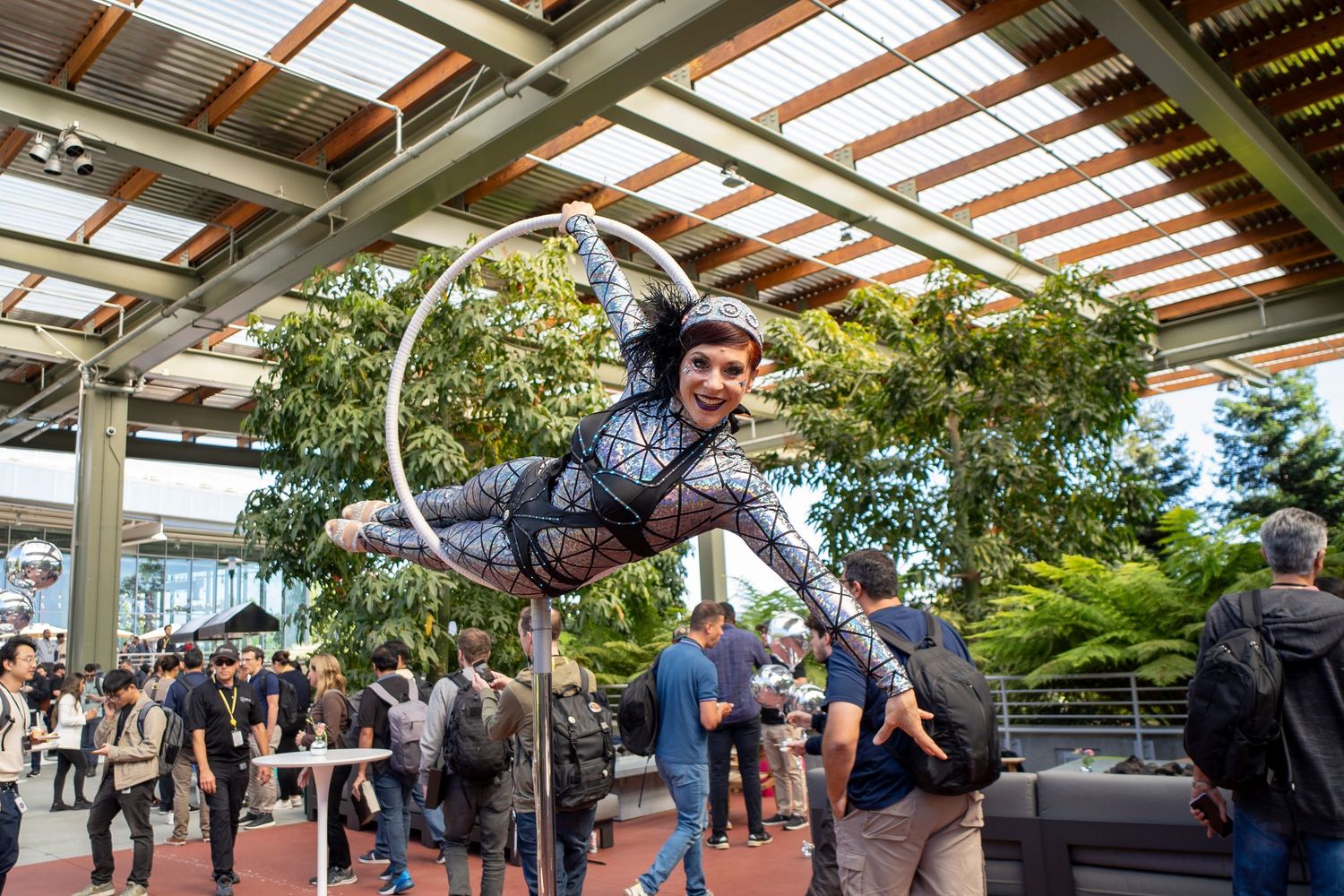 Performer doing an aerial acrobatic display on a ring under a covered outdoor space.
