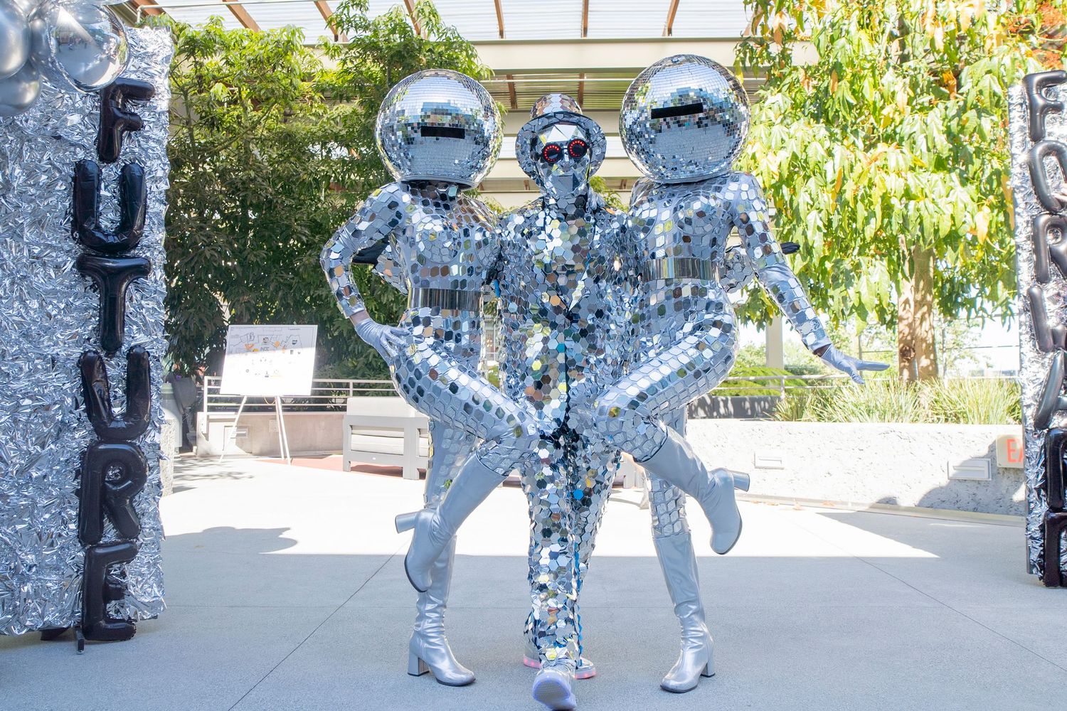 Three mirror-ball costumed performers posing in a bright outdoor setting.