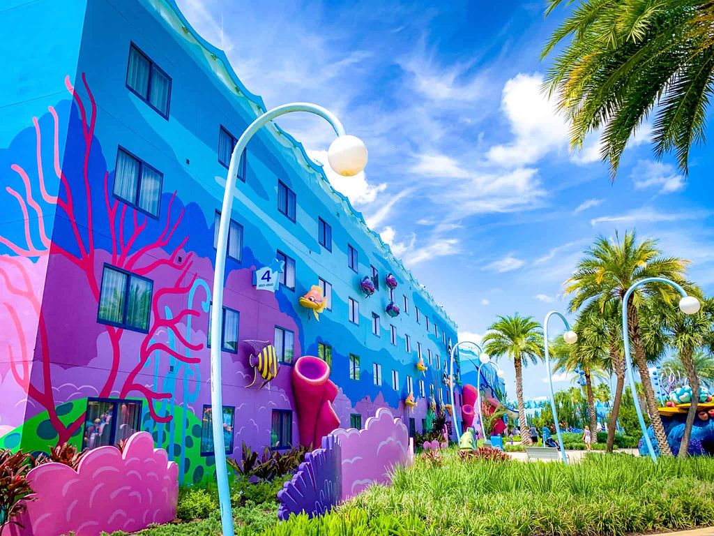 Vibrant blue and pink Art of Animation Resort building exterior with palm trees.