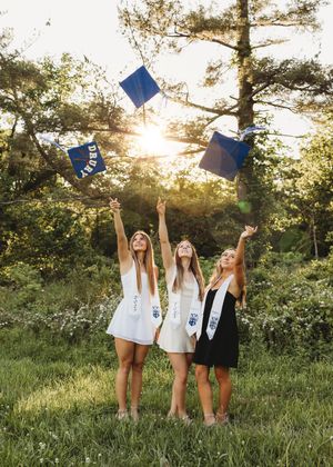 3 friends graduating blue gowns  tossing caps sunset