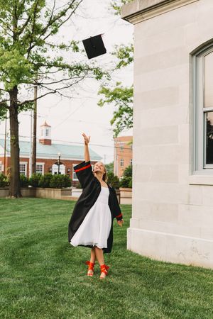 senior graduate girl blonde hair white dress black cap and gown red tassel tossing cap