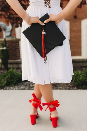 senior graduate girl blonde hair white dress black cap and gown red tassel