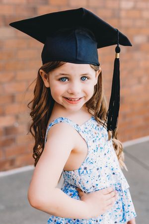 kindergarten cap and gown girl in blue and white shirt blue eyes brown hair black cap and tassel