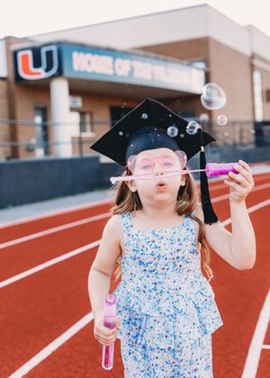 kindergarten cap and gown girl blowing bubble pink heart glasses