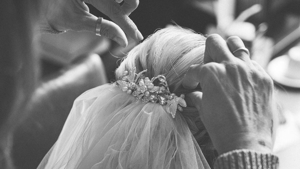 A person carefully adjusts delicate beaded hair accessories and a veil in a black and white close-up shot.