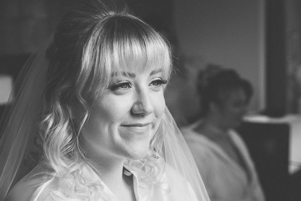 A black and white portrait of a bride with a soft smile wearing a white veil and looking to her left.