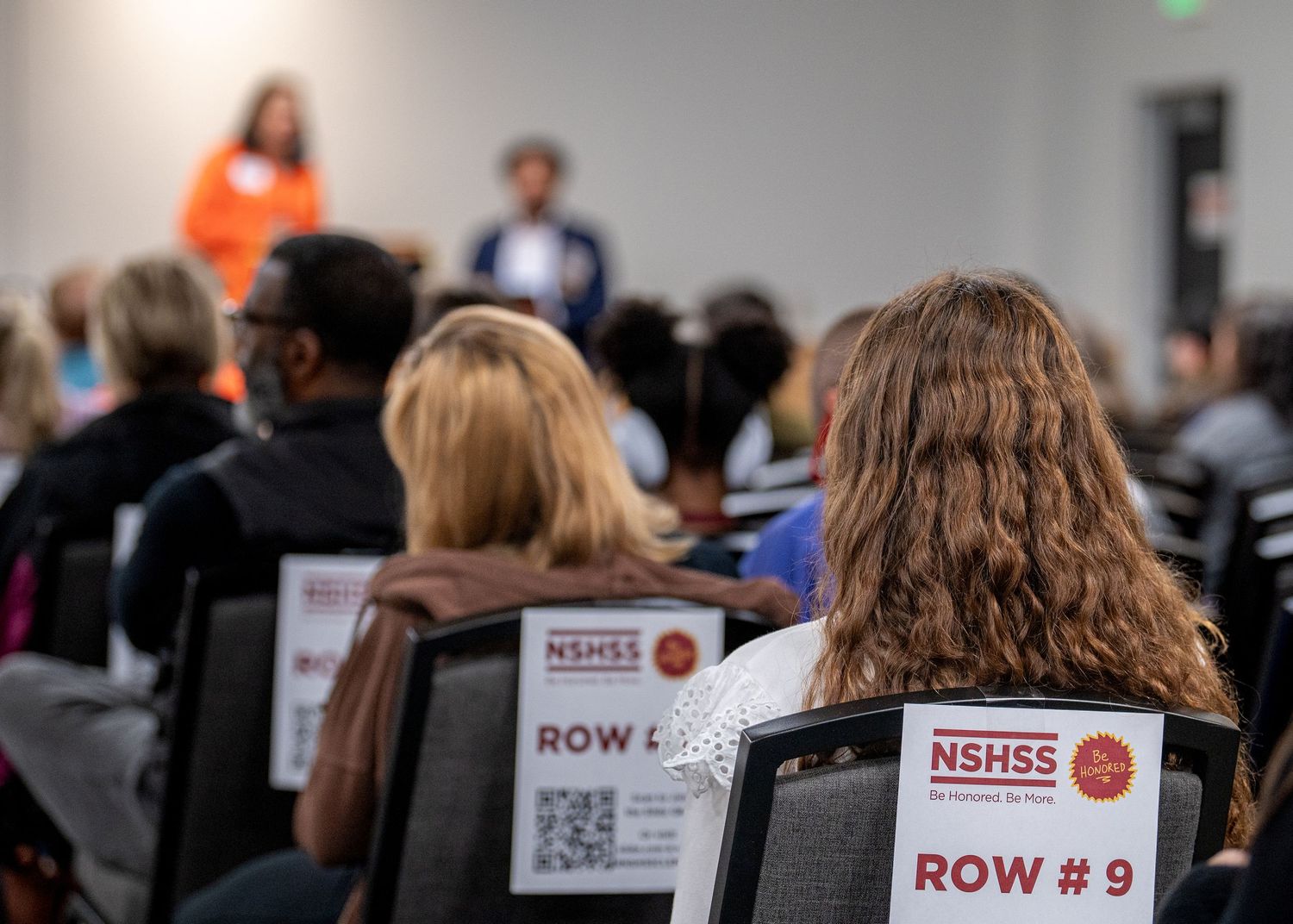 Conference attendees seated in rows with NSEEG event badges visible.