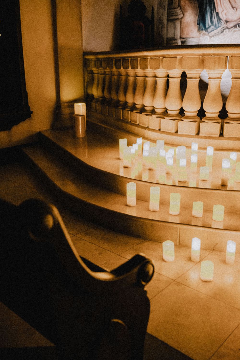 Glowing white candles arranged on curved church altar steps in warm candlelight.