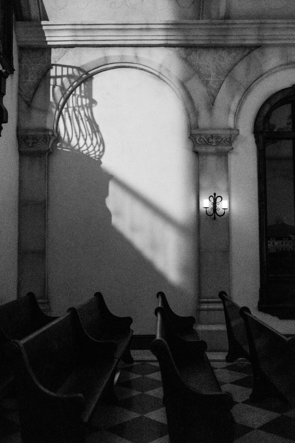 Black and white church interior with ornate arches, pews, and dramatic light and shadow.