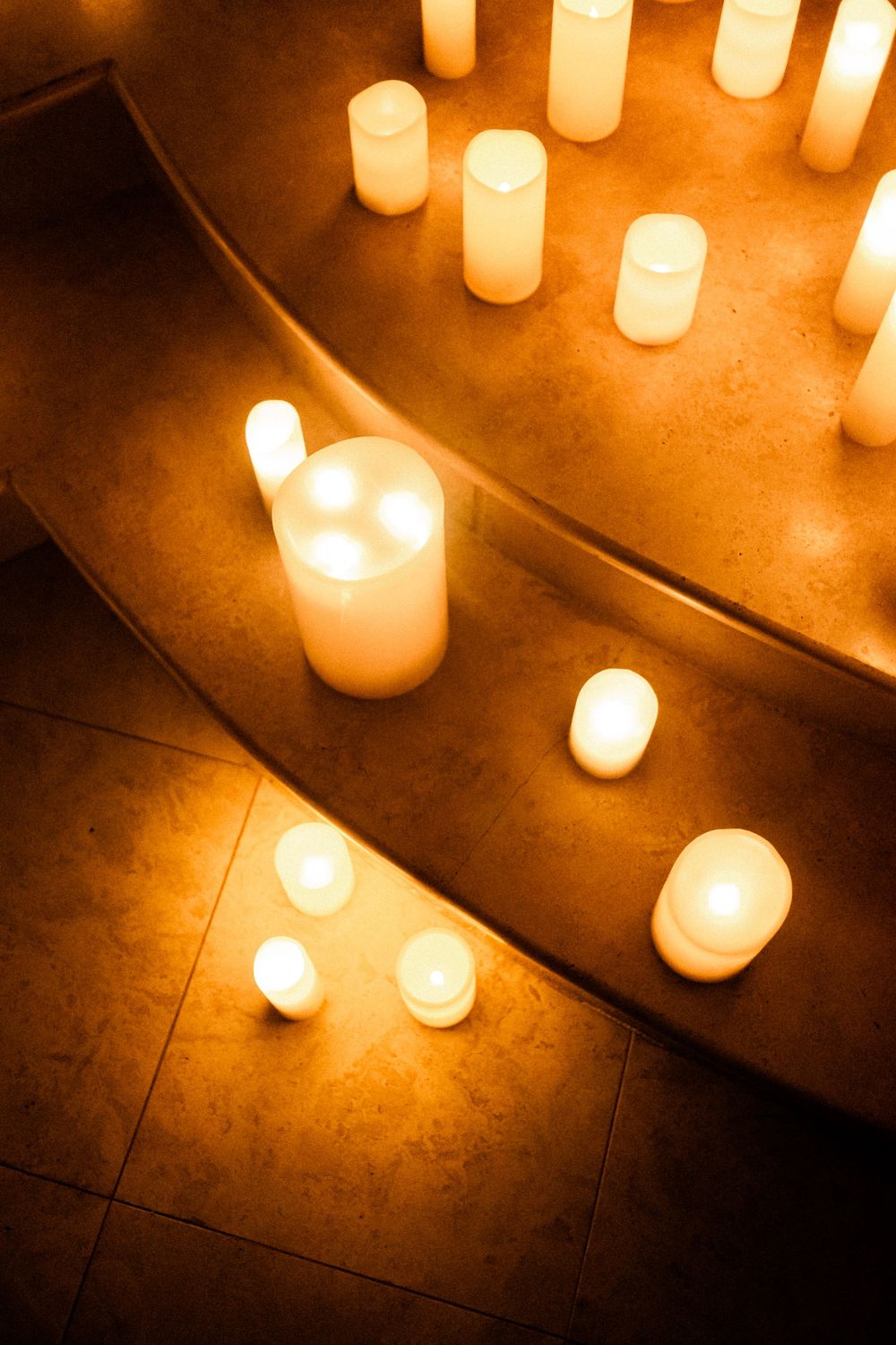 Warm glowing white pillar candles arranged on curved marble church altar steps.