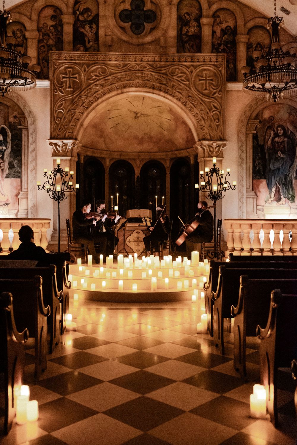 String quartet performing surrounded by hundreds of glowing candles in ornate church interior.