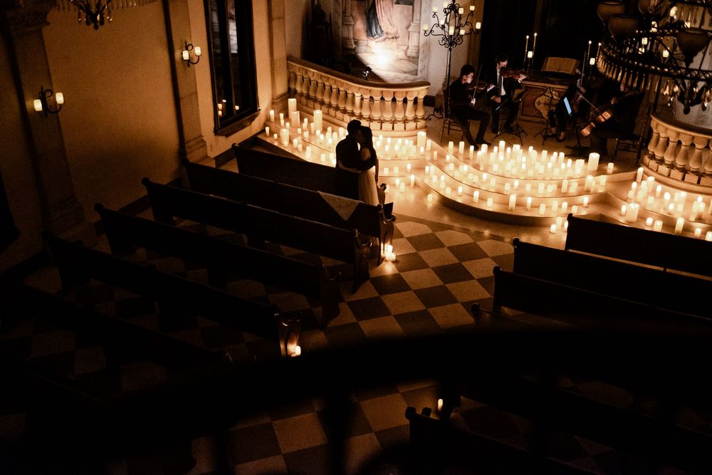 Aerial view of a candlelit church ceremony with rows of glowing candles lining the aisle and a couple embracing.