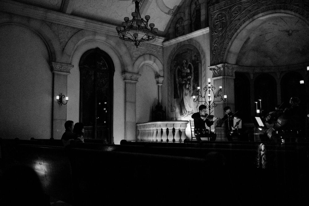 Black and white wide angle shot of string quartet performing in candlelit historic church.