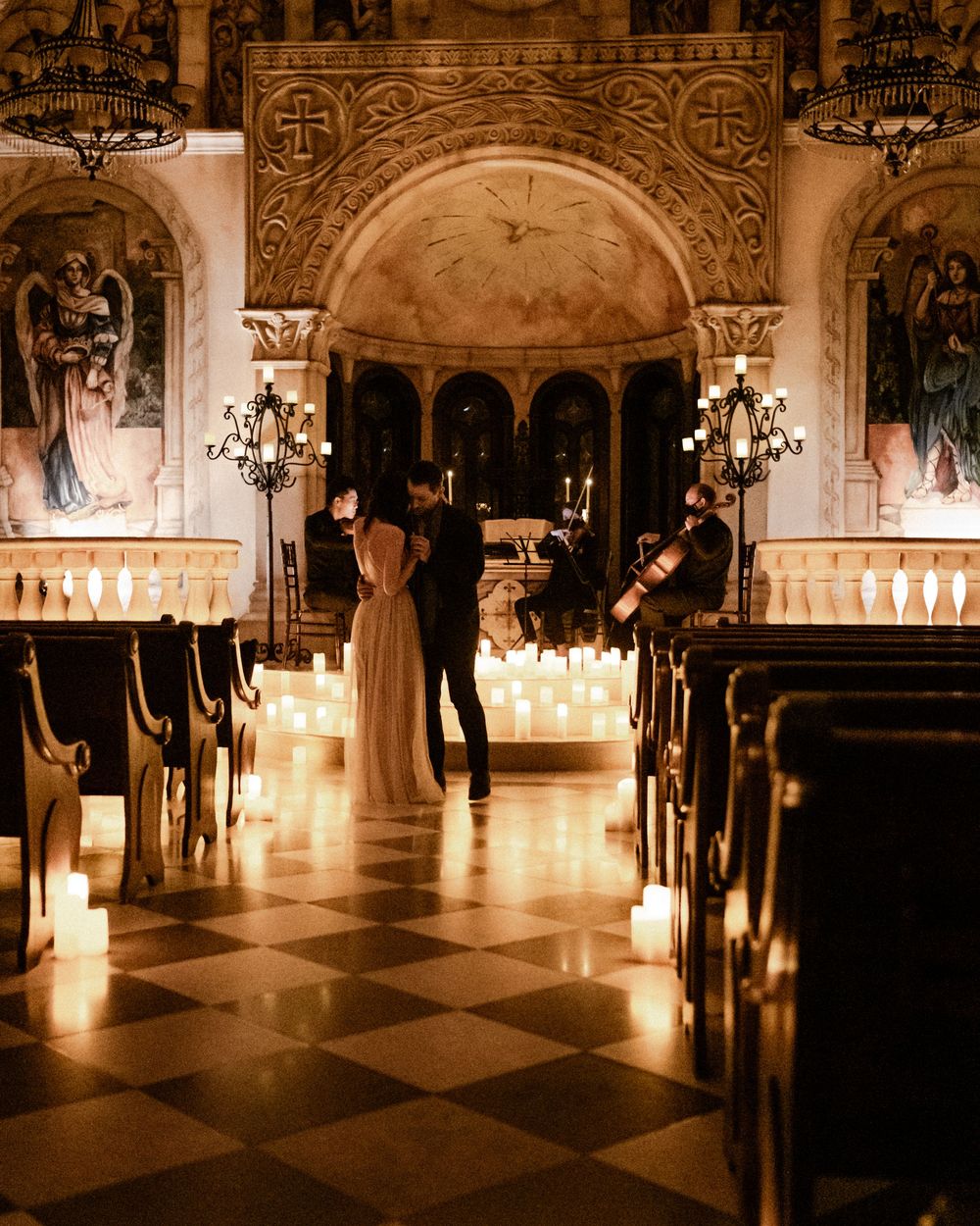 Couple sharing a romantic moment in a candlelit ornate church with a string quartet performing nearby.