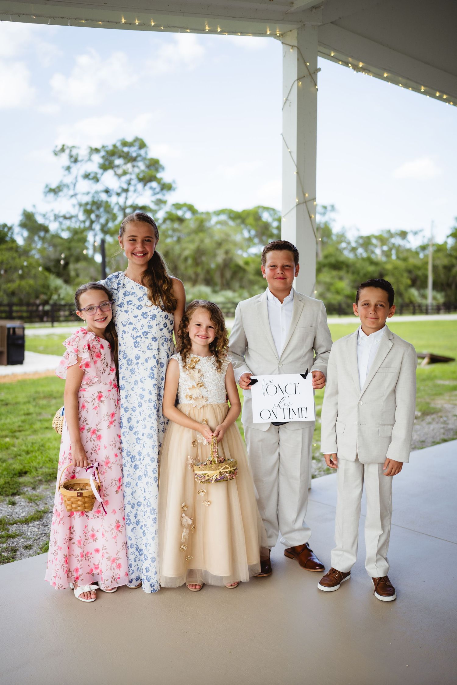 A group dressed in formal attire poses together at an outdoor event under a covered porch.