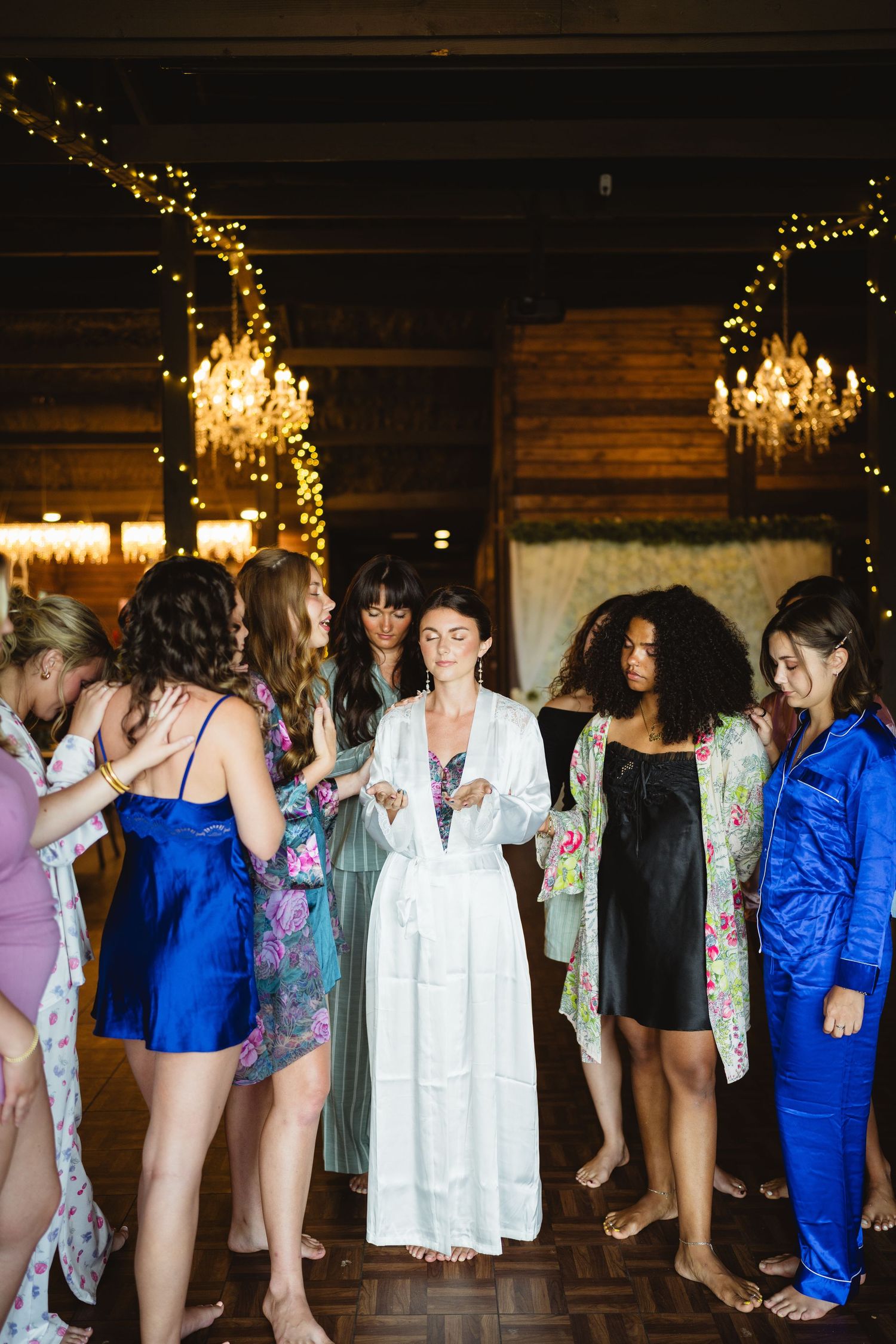 A group of people stand together in a rustic venue with wooden walls and hanging chandeliers at a social gathering.