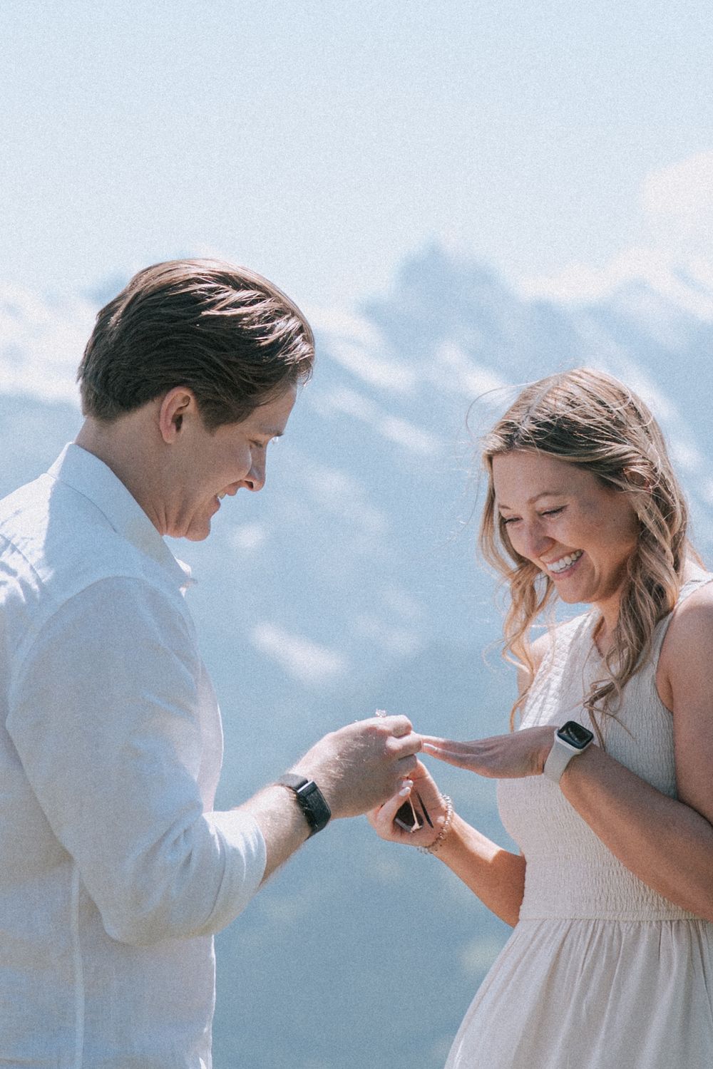 Couple sharing a joyful moment during a mountain proposal with snowy peaks in the background.