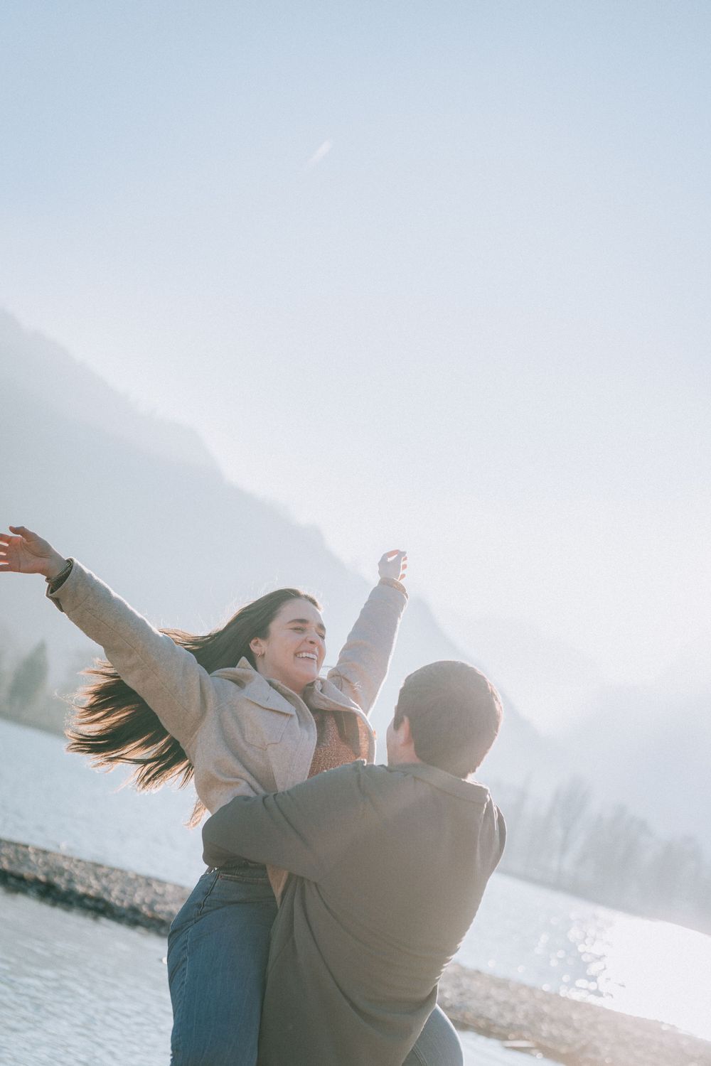 Couple celebrating their engagement by spinning at a lakeside mountain location.