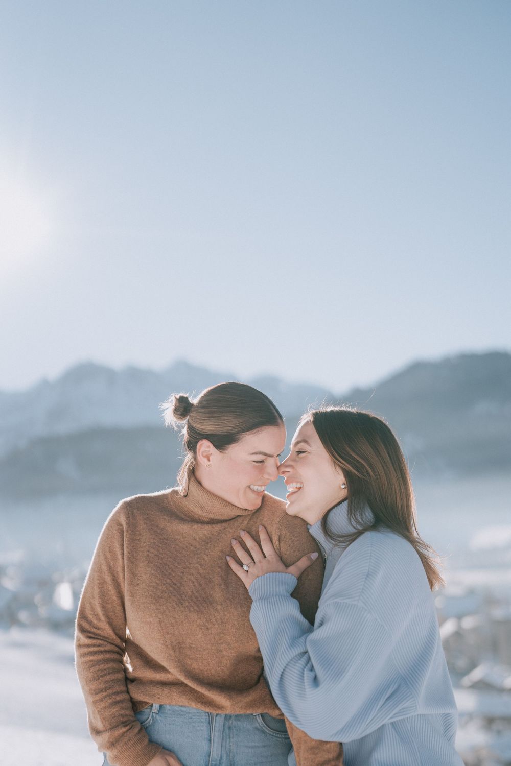 Two people sharing a tender moment while laughing in a snowy mountain setting.