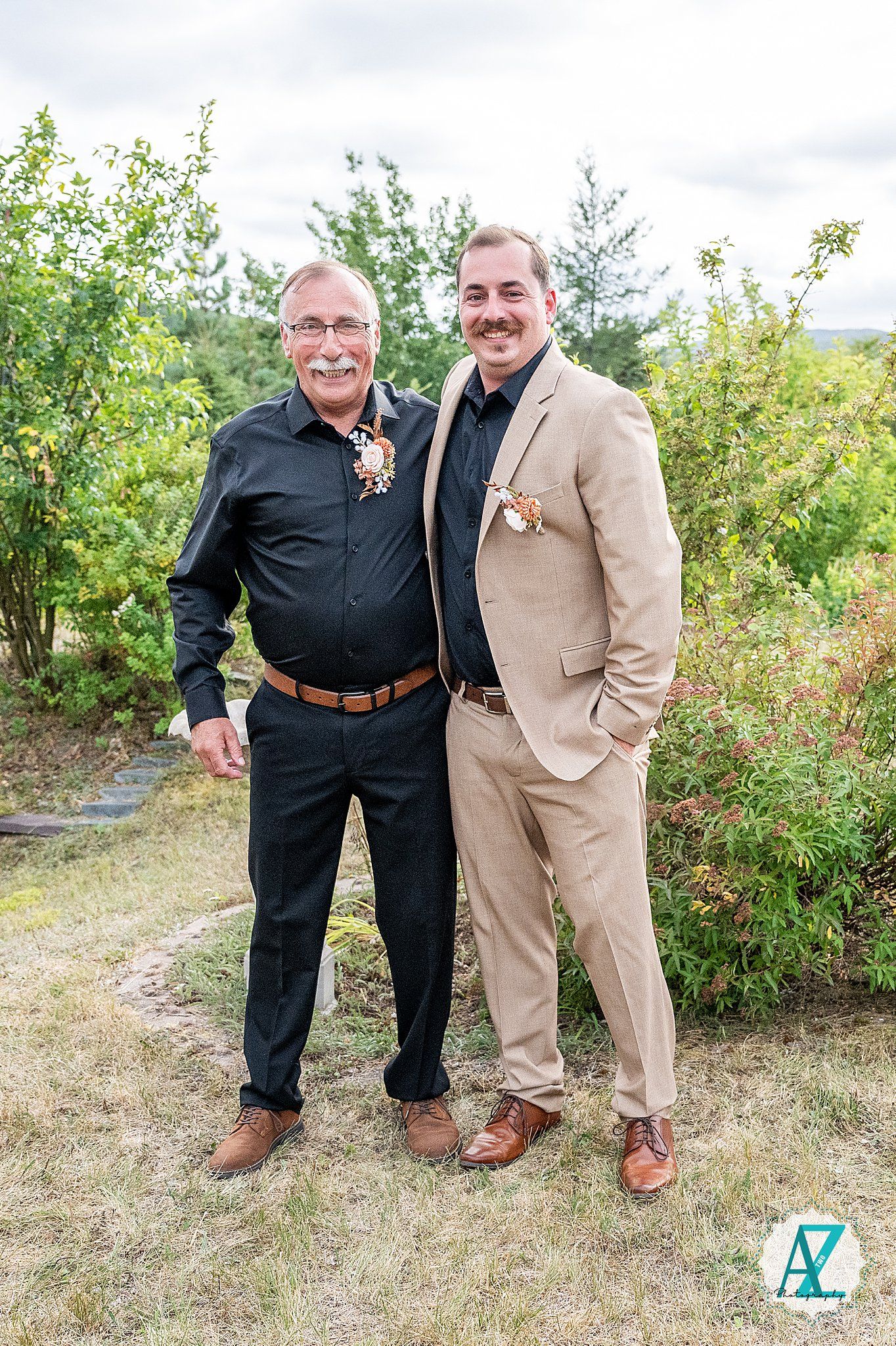 Formal portrait of two men in contrasting black and tan suits with matching boutonnieres.